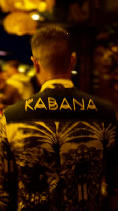 Staff member wearing a Kabana branded palm-print shirt — seen from behind