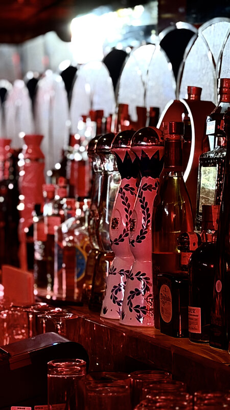 Bar bottles under red light late at night at Kabana — Johnnie Walker bar mat, near-empty glasses
