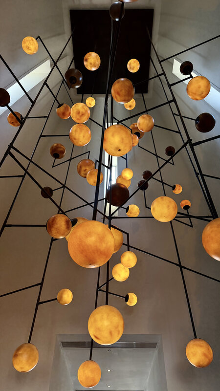 Hanging golden orb sculpture in a clubhouse atrium — globes suspended from a black wire frame