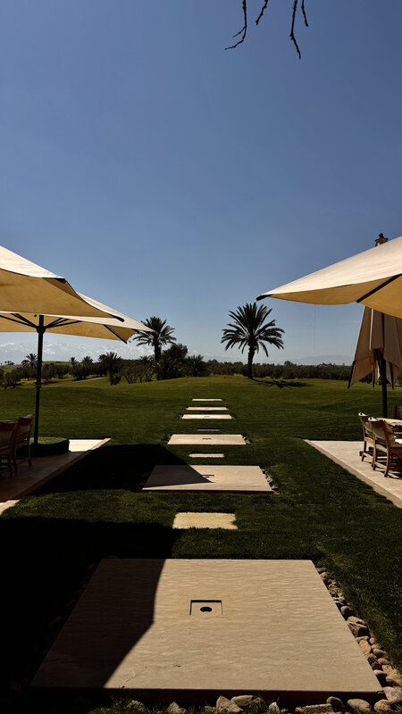 Walkway out from the Assoufid clubhouse — stepping stones, white parasols on both sides, a lone palm in the distance