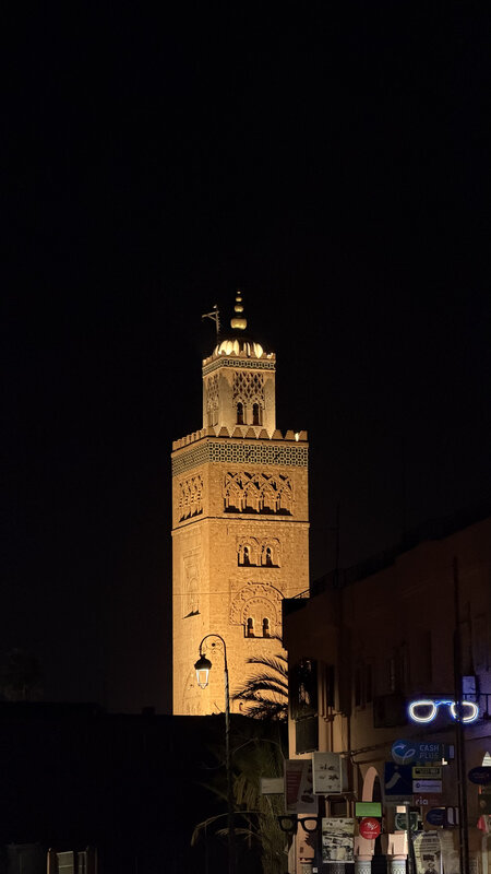 Koutoubia Mosque minaret lit at night above Marrakesh — palm tree silhouette in the foreground