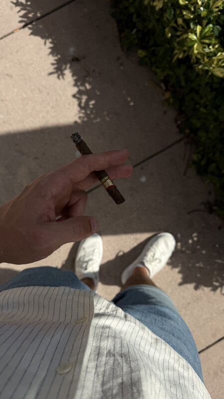 Cigar in hand on a sunny Miami sidewalk — white sneakers and striped linen