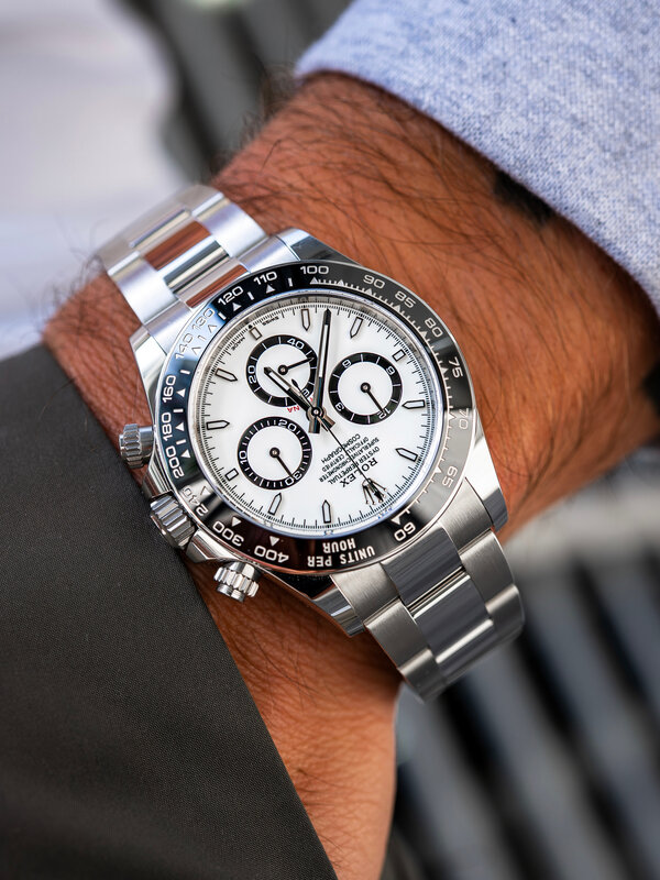 Rolex Daytona with white dial and steel bracelet on wrist over light grey trousers