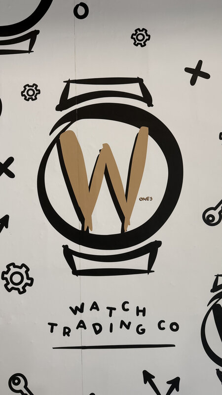 Watch Trading Co brand mural — large 'W' logo and brand name painted on a white wall, surrounding watch icons