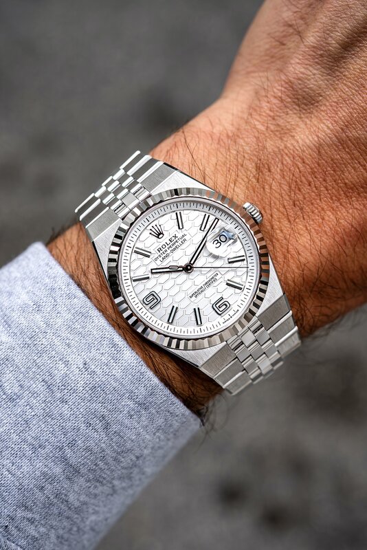 Rolex Datejust with white dial and Jubilee bracelet on wrist — grey jacket, outdoor light