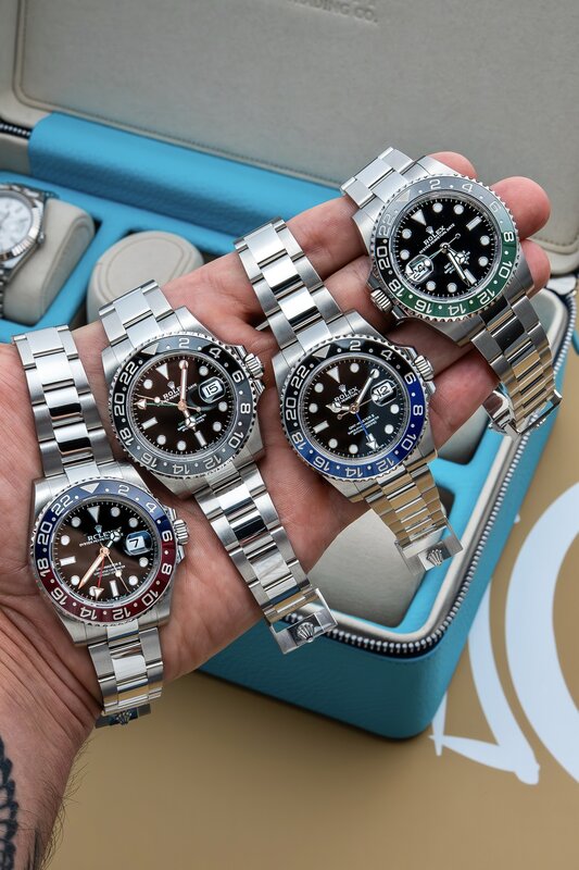 Four Rolex GMT-Master II watches held in a hand — Pepsi, Sprite, Batman, two-tone Root Beer bezels