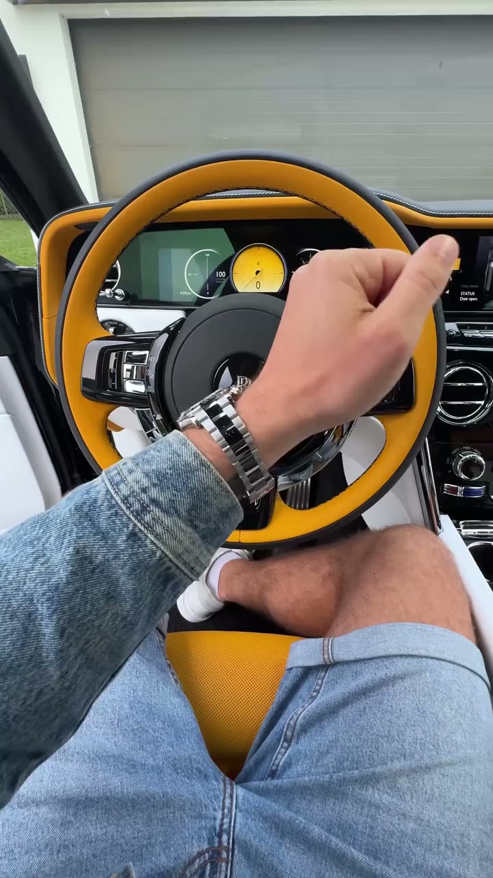 Inside a Rolls-Royce Cullinan with custom canary yellow leather interior — view of steering wheel, twin digital dashboard, and Rolex Daytona on the driver's wrist — video