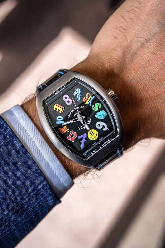 Franck Muller Crazy Hours in a black PVD tonneau case worn on the wrist, black dial with scrambled multicolour numerals and playful symbols, blue leather strap