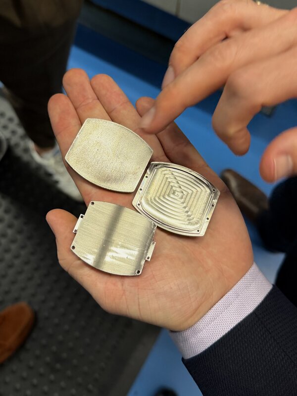 A hand holding three raw tonneau case blanks in the workshop, one machined with a concentric guilloché-style pattern
