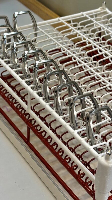Rows of polished tonneau case middles resting in a red-and-white coated wire drying rack inside the manufacture