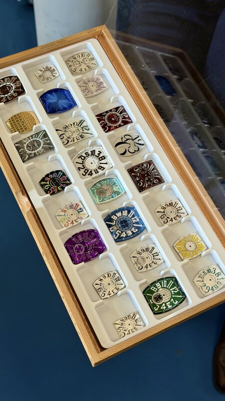 A wooden tray of colourful prototype Crazy Hours dials displayed under a glass lid