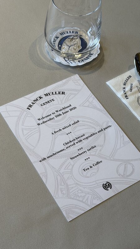 The Watchland lunch menu card reading Franck Muller Genève, Welcome to Watchland, Wednesday 10th June 2026, beside a tumbler with a watch-dial coaster