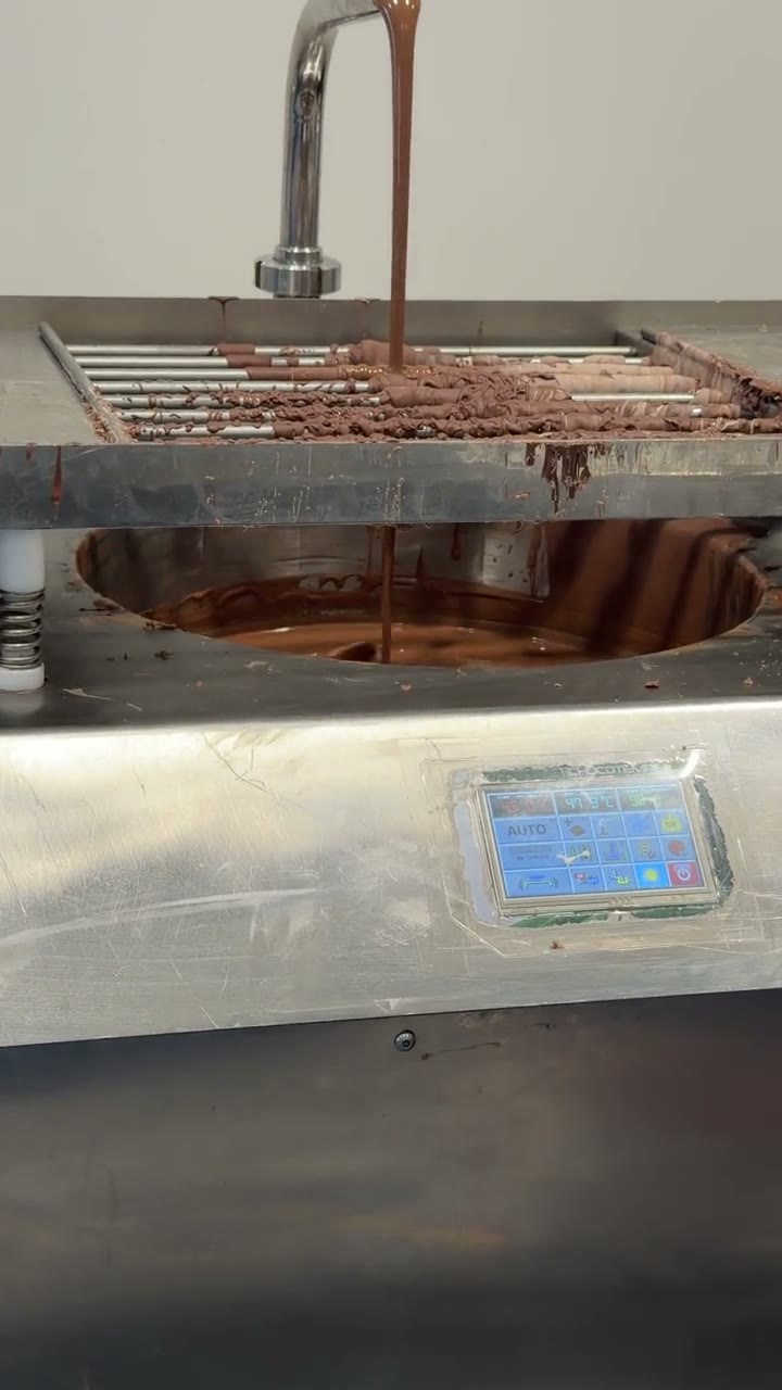 A stainless tempering machine at the Watchland lunch, pale cream then dark glossy chocolate flowing over a grid into a tray