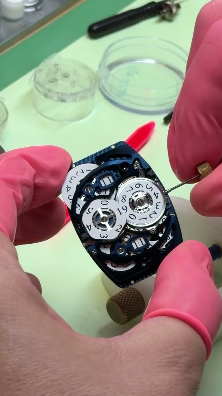 An uncased skeletonised Franck Muller tonneau movement held in finger cots, the crown turning its white printed numeral display discs
